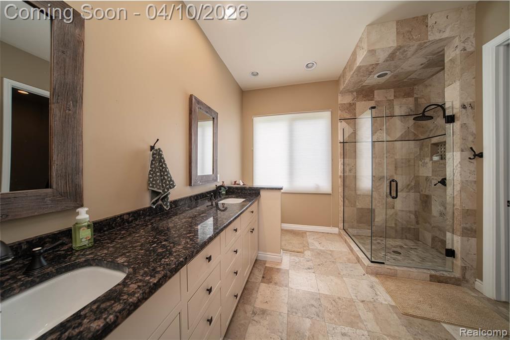 Full bath featuring double vanity, a stall shower, light stone finish flooring, and recessed lighting