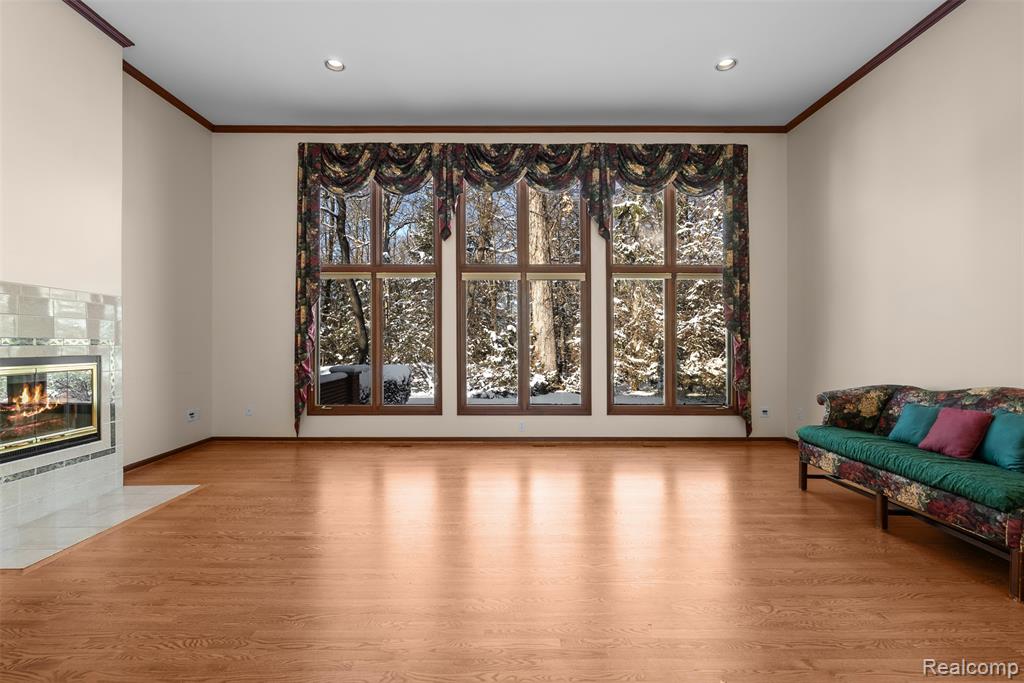Living area with a tiled fireplace, light wood finished floors, ornamental molding, and recessed lighting