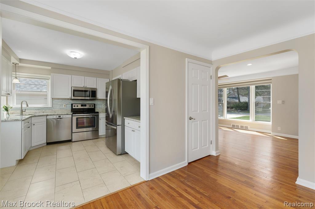 Kitchen with stainless steel appliances, white cabinetry, decorative backsplash, and light stone countertops