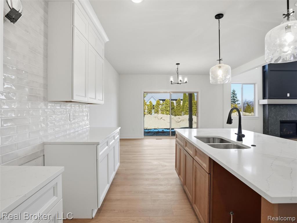 Dual tone kitchen with light stone counters, a fireplace, light wood finished floors, two tone cabinets, and a center island with sink