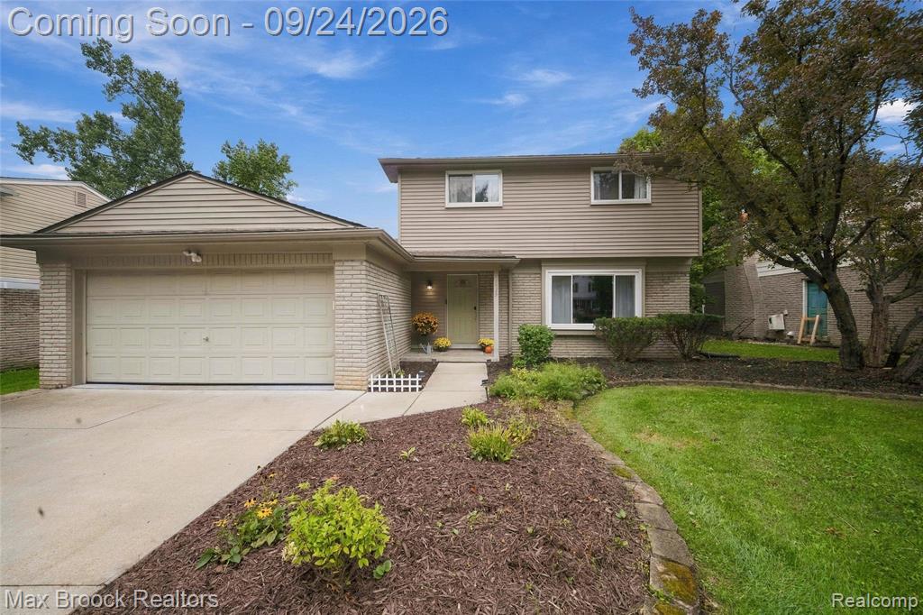 Two-story exterior with horizontal siding and brick accents, featuring a two-car garage with an overhead door, a concrete driveway, and a landscaped front yard with a walkway