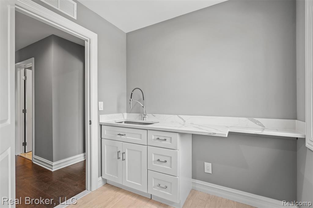 Bar with light stone counters, light wood-style floors, and white cabinets