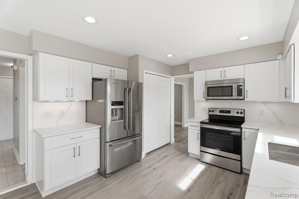 Kitchen with stainless steel appliances, white cabinets, light stone countertops, recessed lighting, and light wood-type flooring