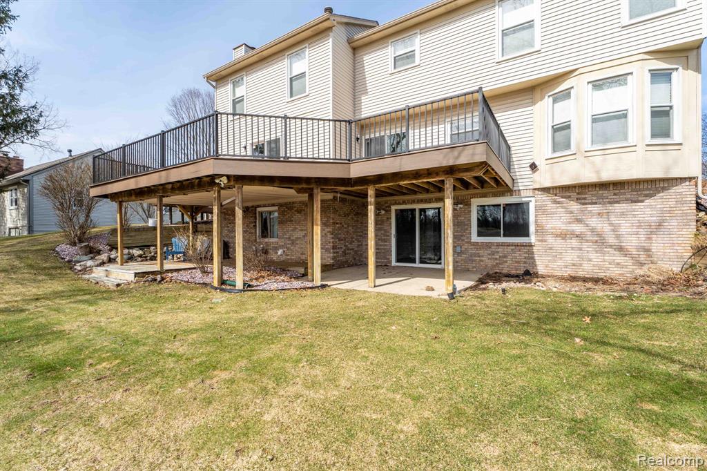 Rear view of house featuring brick siding, a deck, a patio area, and a yard