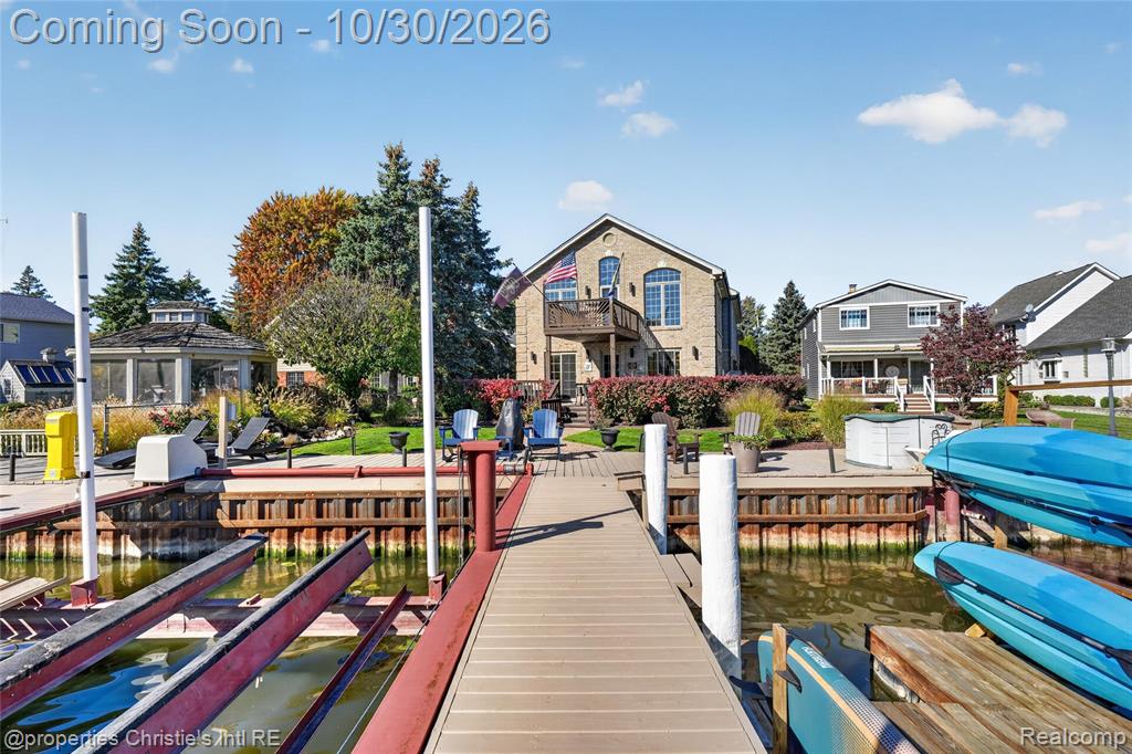 Waterfront residence featuring a private boat dock, multi-level exterior decking, stone facade, and paved patio area