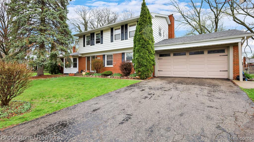 Colonial inspired home with brick siding, asphalt driveway, a garage, a front lawn, and a chimney