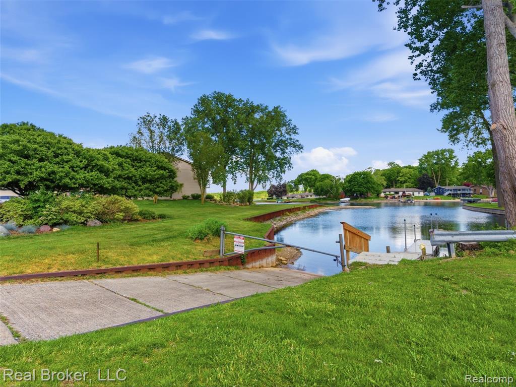 Expansive waterfront property featuring a wide body of water, green grassy shore, mature trees, and a wooden dock structure