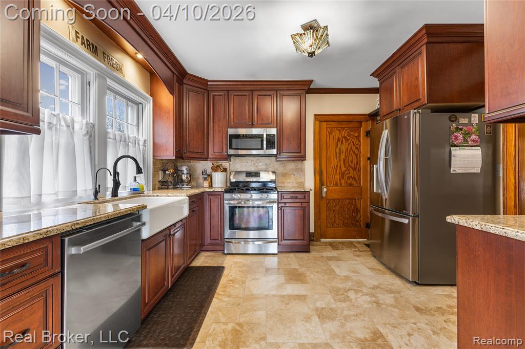 Kitchen featuring stainless steel appliances, crown molding, light stone counters, tasteful backsplash, and stone finish flooring