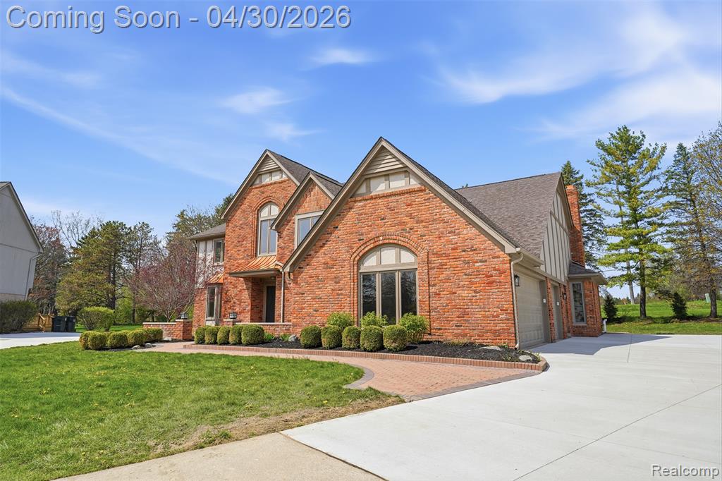 View of front of home with a front lawn, brick siding, concrete driveway, a garage, and roof with shingles