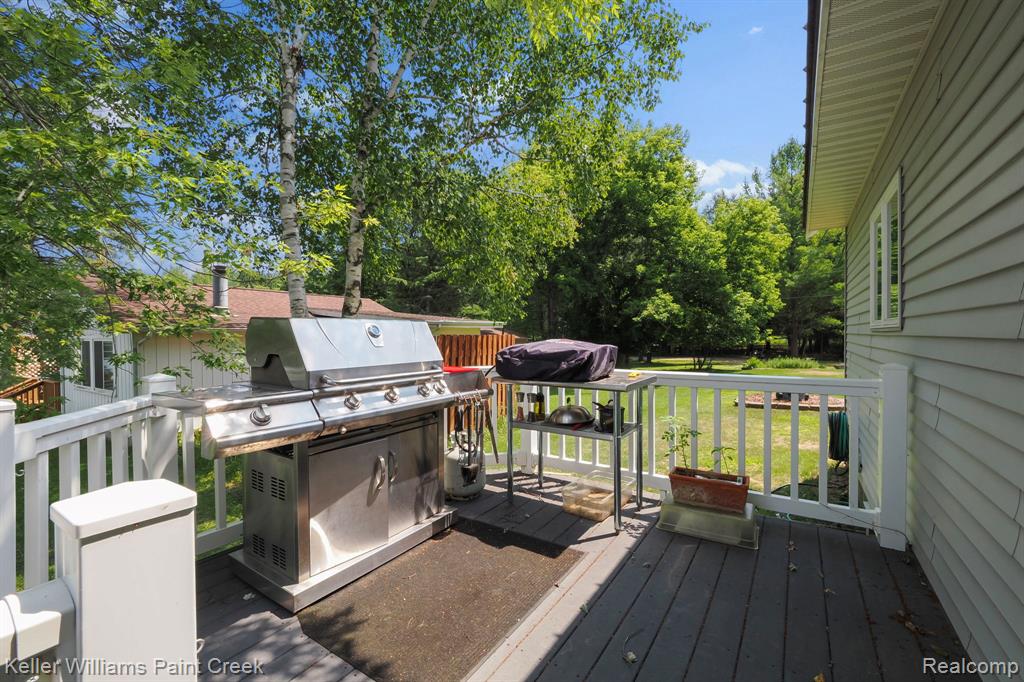 Exterior deck with white railing, gray siding, and surrounding mature trees