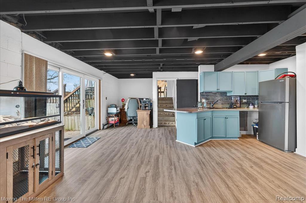 Kitchen featuring freestanding refrigerator, light countertops, a peninsula, light wood-style floors, and blue cabinets