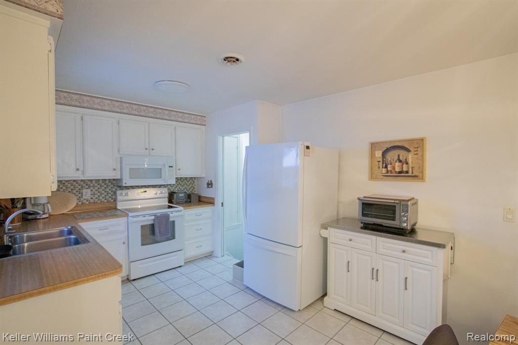 Kitchen with white appliances, white cabinetry, light tile patterned flooring, light countertops, and tasteful backsplash