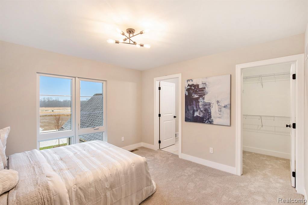 Bedroom featuring a walk in closet, a chandelier, and light carpet