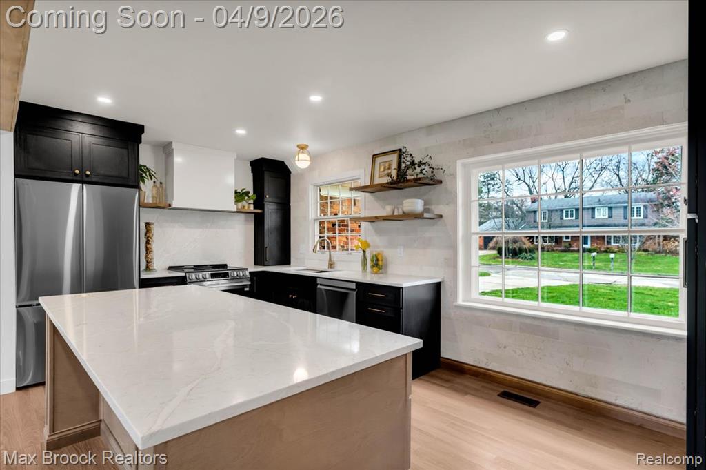 Kitchen featuring dark cabinetry, stainless steel appliances, light stone countertops, open shelves, and a kitchen island