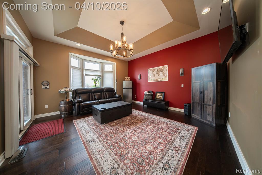Living room with a tray ceiling, a chandelier, and dark wood-style flooring