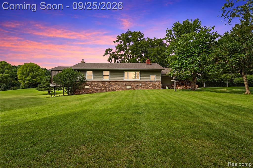 Expansive green lawn, mature trees, and a house featuring a brick and siding exterior, a gabled roof, and multiple windows