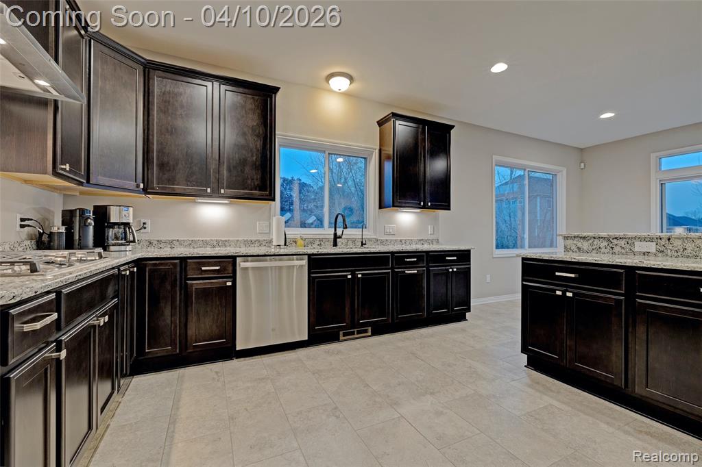 Kitchen featuring stainless steel dishwasher, light stone countertops, recessed lighting, dark wood finish cabinets, and healthy amount of natural light