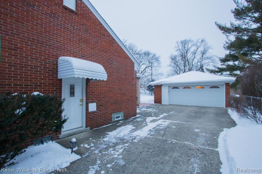 Snow covered property featuring an outbuilding, brick siding, and a garage