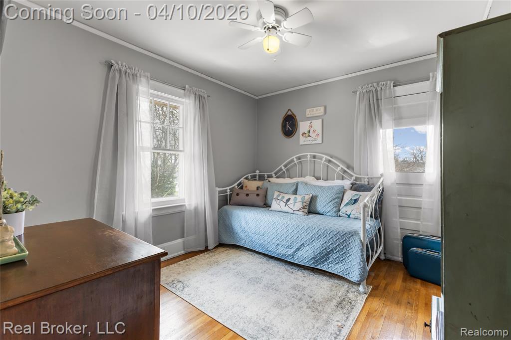 Bedroom with light wood-type flooring, ceiling fan, multiple windows, and ornamental molding
