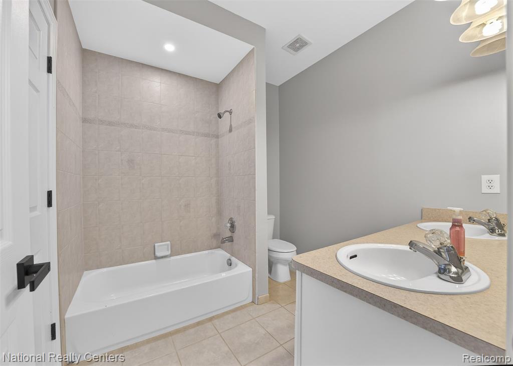Bathroom with double vanity, tub / shower combination, light tile patterned flooring, and recessed lighting