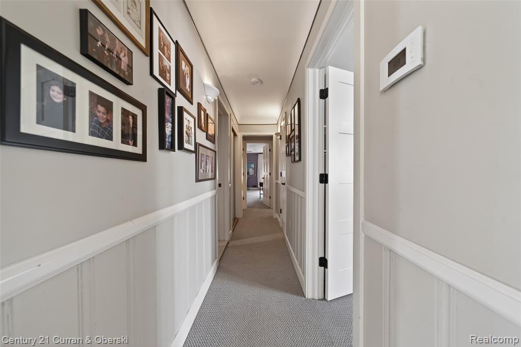 Hall featuring a decorative wall, light colored carpet, and wainscoting