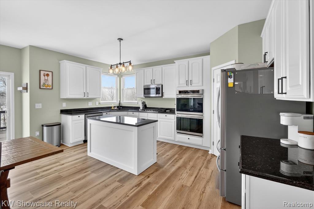 Kitchen featuring white cabinets, decorative light fixtures, stainless steel dishwasher, open floor plan, and plenty of natural light