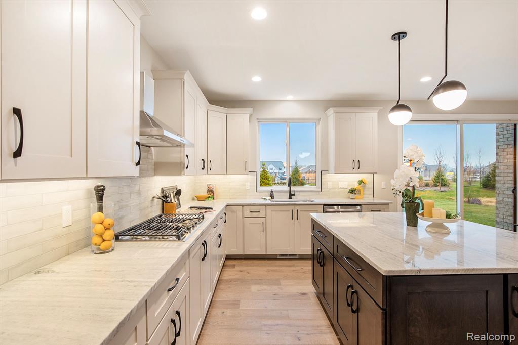 Kitchen featuring dark brown cabinets, light stone countertops, light wood-style floors, pendant lighting, and recessed lighting