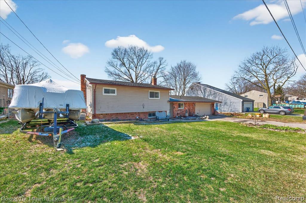 Back of property with a chimney, brick siding, a yard, and an attached garage