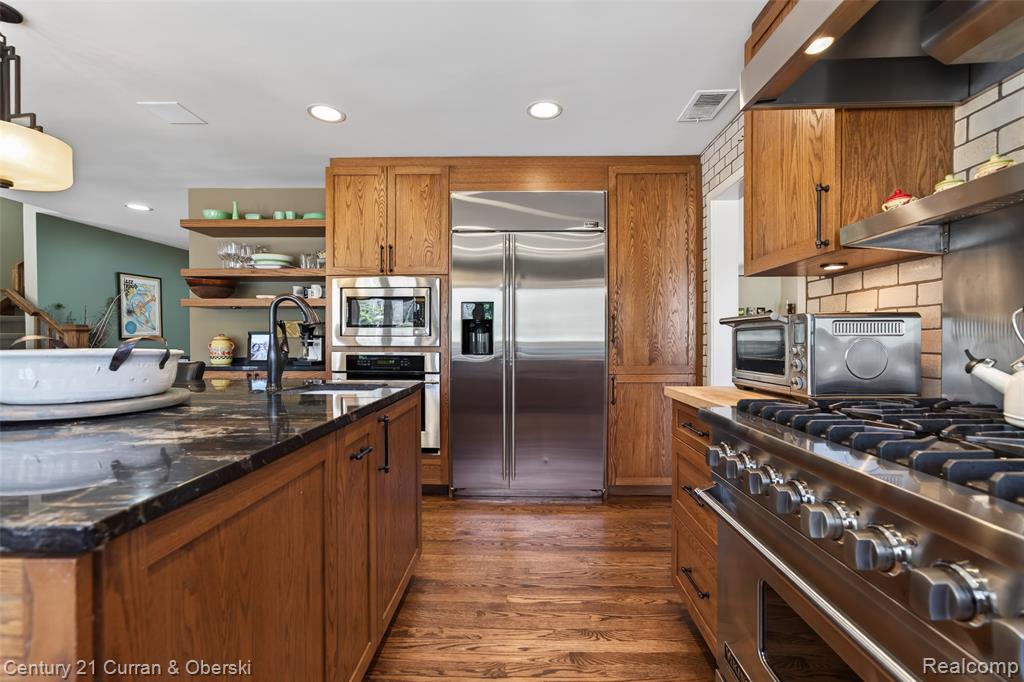 Kitchen with open shelves, built in appliances, wood finish cabinets, and dark wood-style floors