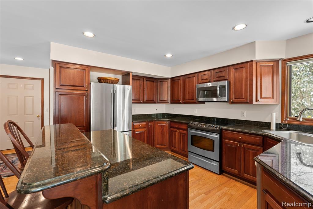 Kitchen featuring appliances with stainless steel finishes, dark stone counters, a kitchen breakfast bar, light wood-style flooring, and recessed lighting