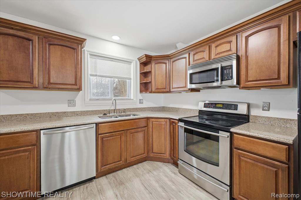 Kitchen with appliances with stainless steel finishes, brown cabinets, open shelves, light stone countertops, and recessed lighting