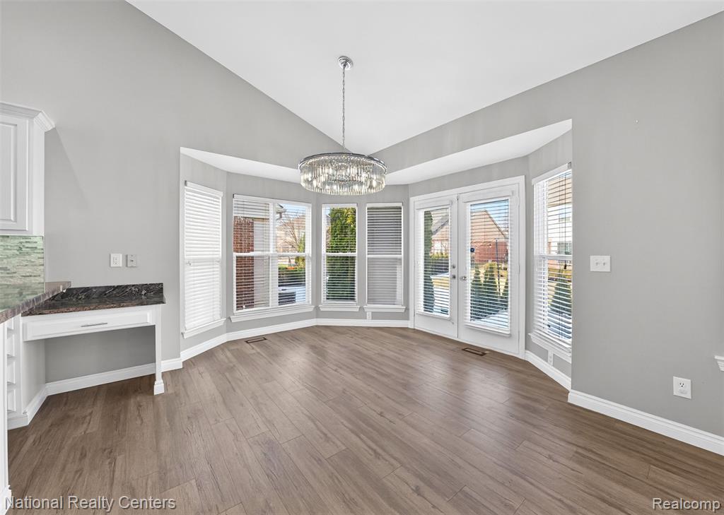 Unfurnished dining area with vaulted ceiling, dark wood-style floors, hanging lights, plenty of natural light, and french doors