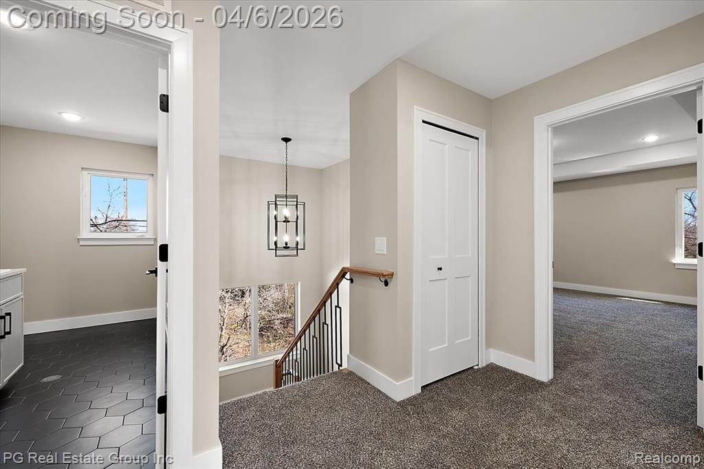 Hall featuring healthy amount of natural light, dark carpet, an upstairs landing, and hanging lights