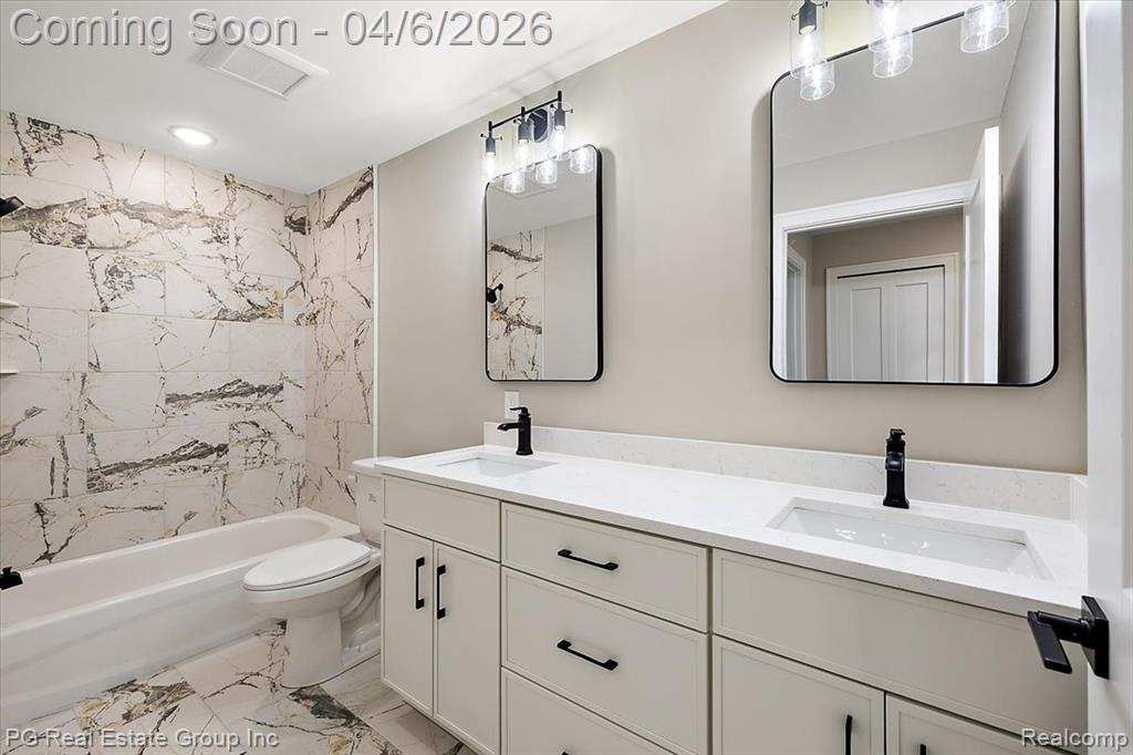 Full bath featuring double vanity, light marble finish flooring, and shower combination