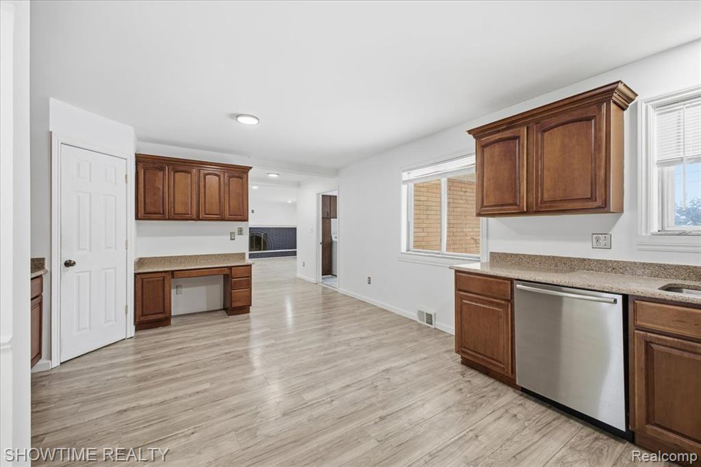 Kitchen with built in desk, stainless steel dishwasher, light stone countertops, and light wood-style floors