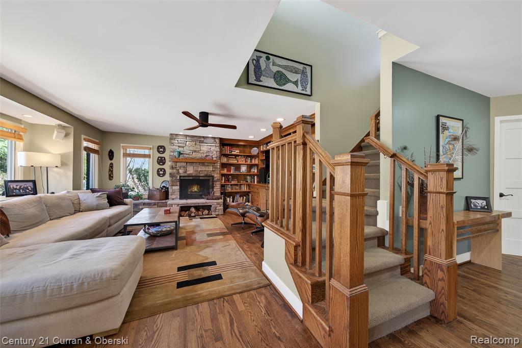 Living room featuring dark wood finished floors, a ceiling fan, a stone fireplace, and recessed lighting