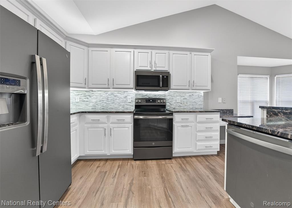 Kitchen with stainless steel appliances, dark stone counters, backsplash, light wood-style floors, and white cabinetry
