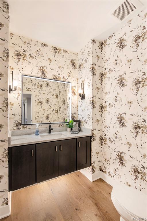 Bathroom with wallpapered walls, vanity, and light wood-style flooring