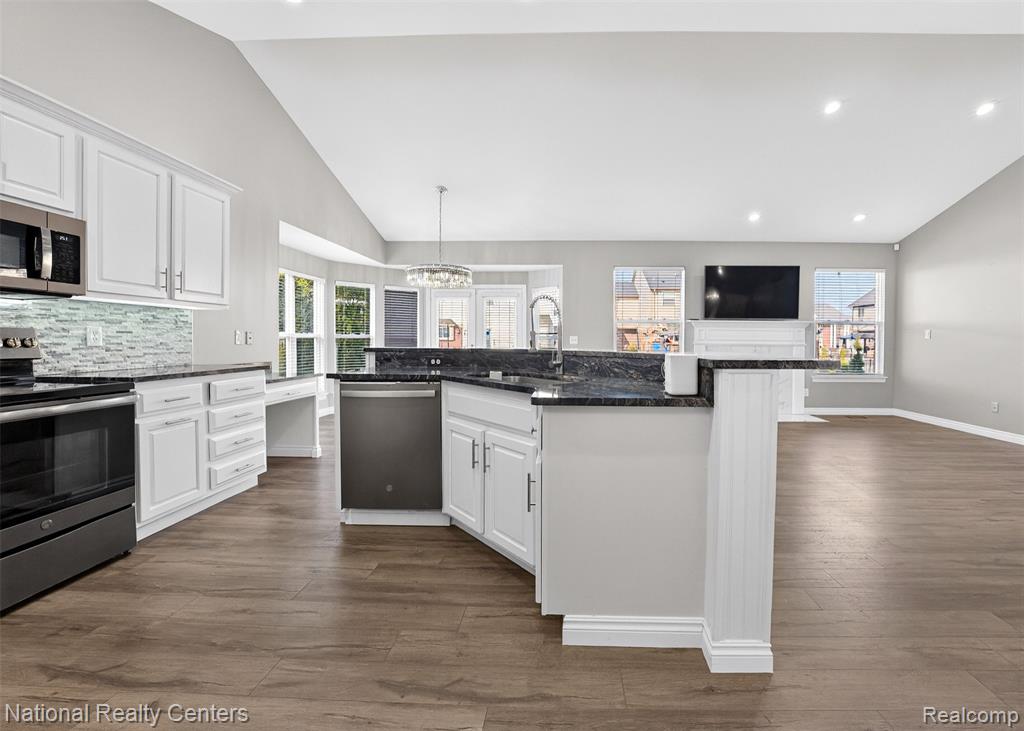 Kitchen featuring white cabinets, vaulted ceiling, stainless steel appliances, and hanging lights