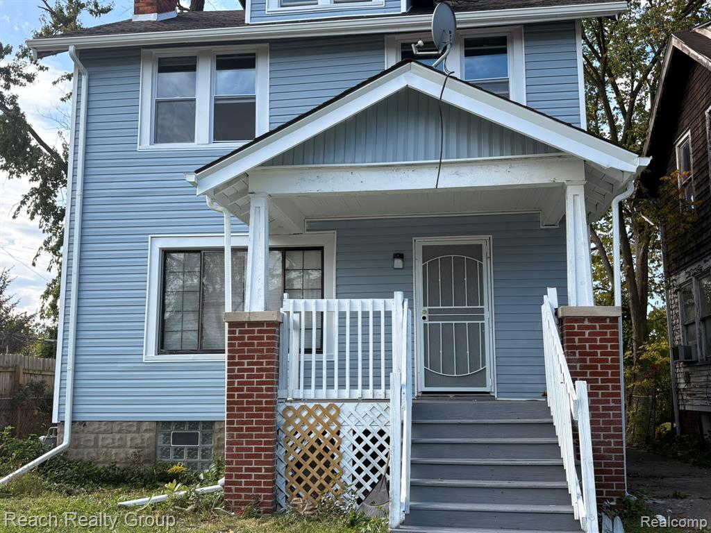 Two-story residence featuring light-blue horizontal siding, a covered front porch with brick pillars, white railing, and a stone foundation