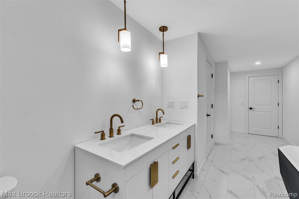 Full bathroom with double vanity, light marble finish floors, a freestanding bath, and recessed lighting