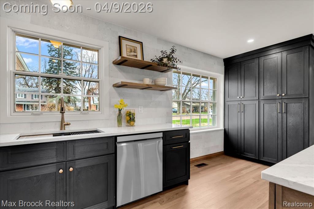 Kitchen featuring dishwasher, light stone counters, light wood finished floors, open shelves, and dark cabinets