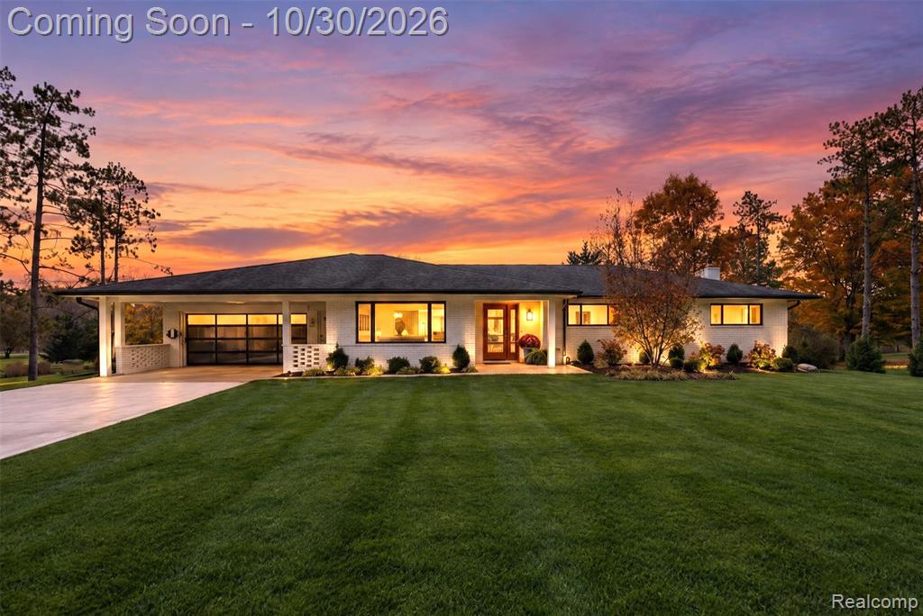 Single-story residence featuring a painted brick exterior, covered parking, horizontal glass-paneled garage door, expansive front lawn, and mature landscaping