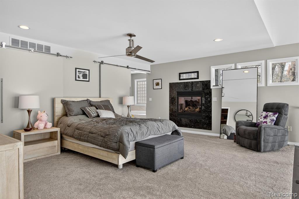 Carpeted bedroom featuring recessed lighting, a ceiling fan, a fireplace, and a barn door