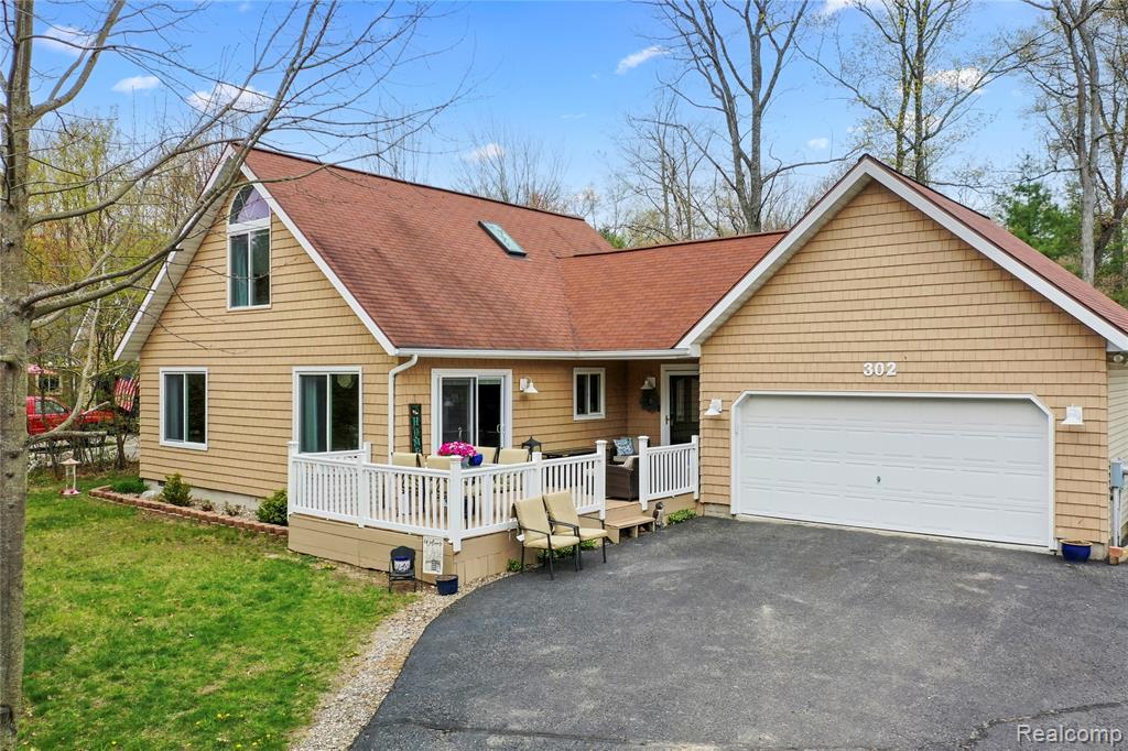 View of front of home featuring a deck, asphalt driveway, a shingled roof, a front lawn, and a garage