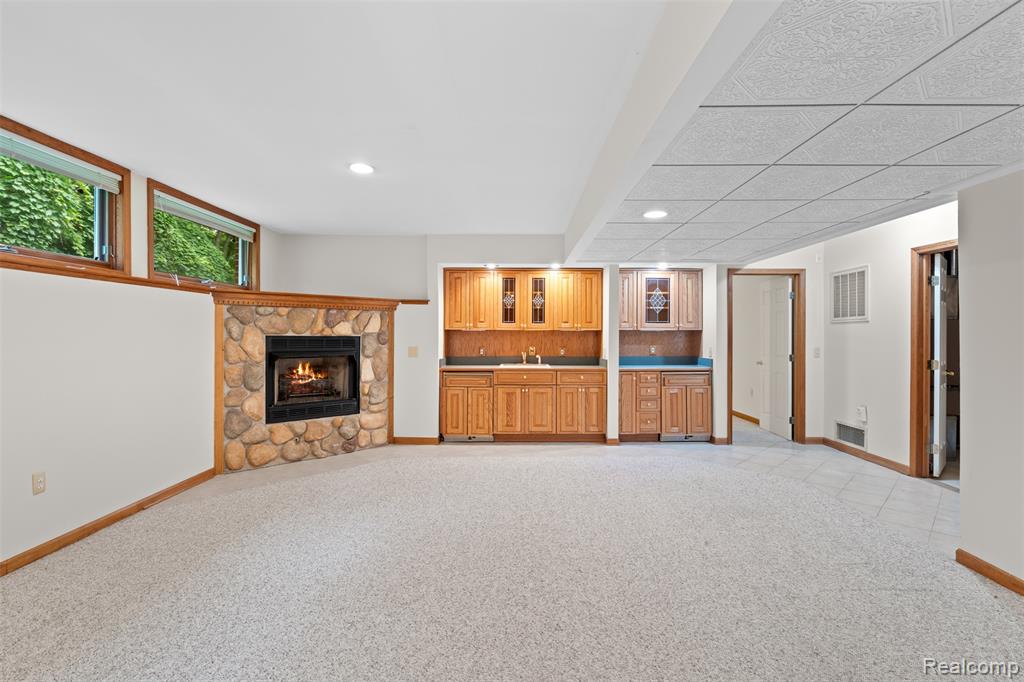 Unfurnished living room with light carpet, a stone fireplace, bar with sink, and recessed lighting