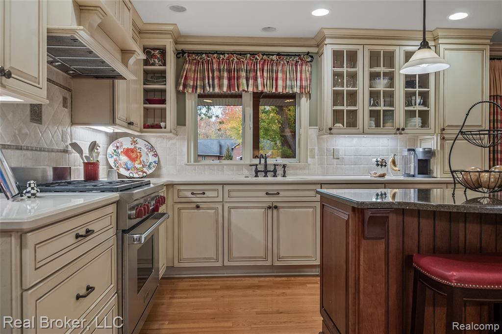Kitchen with cream cabinetry, luxury stove, backsplash, custom range hood, and light wood-style flooring