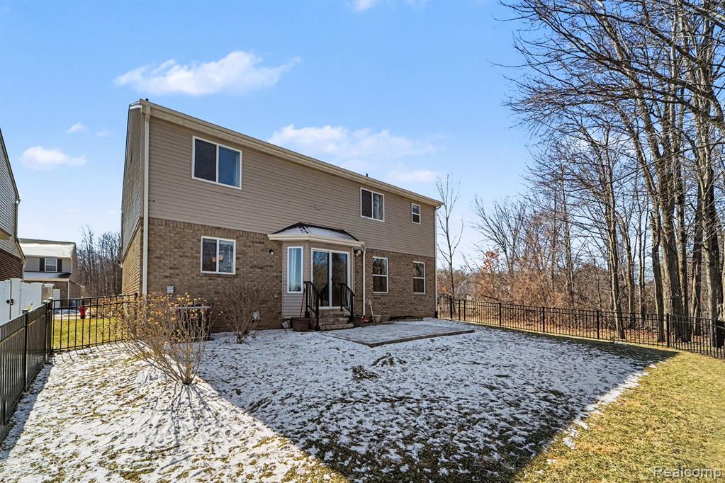 Snow covered back of property featuring brick siding, a fenced backyard, and entry steps
