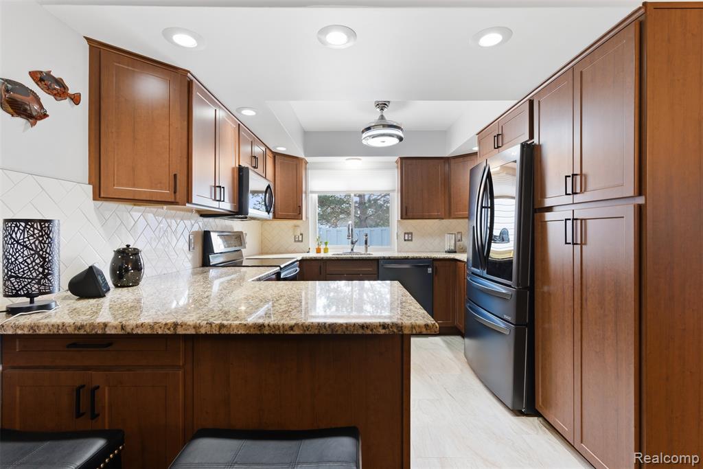 Kitchen with a peninsula, light stone countertops, recessed lighting, stainless steel appliances, and wood finish cabinets