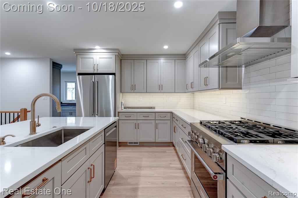 Kitchen with high end appliances, wall chimney range hood, light wood-style flooring, recessed lighting, and light stone counters